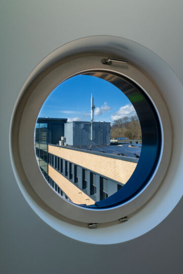 Neubau Geschäftshaus STIRAG - Rundfenster mit Blick auf Photovoltaikanlagen auf dem Flachdach